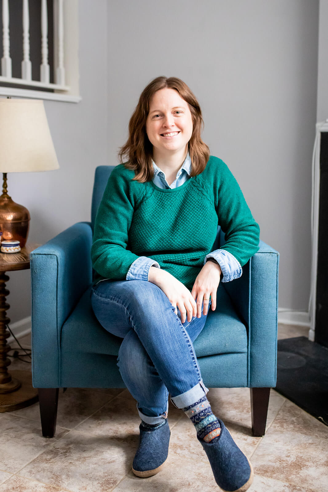 Emily Laing, LPC, a white woman in her mid to late 30s with shoulder-length auburn hair, smiles towards the camera. She wears a grey wool coat over a green sweater and denim collared shirt. She stands outside in front a tree and snow.